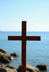 Poster - A wooden cross stands tall near the water, creating a striking silhouette against the tranquil sea. The bright sky and gentle waves evoke a sense of calm and reflection Generative AI