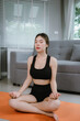 © Natthawadee - A woman practices yoga indoors on a mat, sitting in a relaxed pose. She smiles peacefully, embracing mindfulness, balance, fitness, and a healthy lifestyle at home.