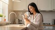 © luwie - Woman using phone drinking coffee in kitchen morning routine lifestyle at home pajamas relaxing indoor