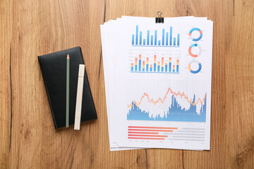 Fototapete - Notebook with stationery, business graphics and diagrams on brown wooden background