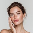 © UnderTheSun - A woman with natural beauty lightly touches her face, showcasing a fresh and radiant complexion against a neutral backdrop.