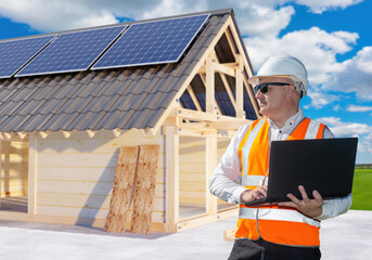 Poster - Builder near energy efficient house. Man architect holding laptop. Construction of house with solar panels on roof. Development of energy efficient housing. Man designer of eco cottage