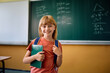 © Drazen - Happy schoolgirl in front of chalkboard looking at camera.