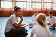 © Drazen - Black female coach and group of kids talking on physical education class at school gym.