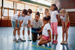 © Drazen - Black sports teacher and her students going through exercise plans at school gym.