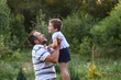 © illustrissima - Happy father and  son playing outside in garden in summer in sun. dad roll son on neck, roll on shoulders, play throws up. involved parenting, time with children. leisure without gadgets. Father's day