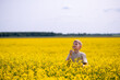 © kazakova0684 - Blond boy standing in a blooming rapeseed field on a sunny day, gently smelling a yellow flower, surrounded by nature and golden light