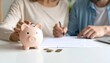 © Nashihal - Saving money concept. Couple reviewing financial documents with a piggy bank on the table, emphasizing savings and financial planning.
