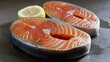 © Maria Mikhaylichenko - Fresh salmon steaks with vibrant orange-pink flesh, showcasing marbled texture and accompanied by a bright lemon slice on a neutral gray surface.