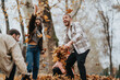 © qunica.com - A cheerful group of friends celebrates a crisp autumn day by playing outside in a park, joyfully throwing vibrant fallen leaves amidst the colorful natural beauty, smiling and full of happiness.