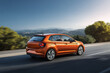 © Mr.Spy - Vibrant orange hatchback driving on a clear road with motion blur, surrounded by lush green hills and a bright blue sky, perfect for showcasing modern automotive design, travel, and the joy of a journ