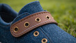 © Mr-Nomi - Close-Up of Denim Shoe with Brown Leather Strap and Brass Eyelets .