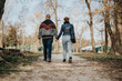 © qunica.com - Two people, a man and a woman, walk hand in hand down a gravel path surrounded by tall trees, enjoying their relaxing stroll in an outdoor park setting.