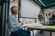 © qunica.com - A young student confidently presents in front of a class while an elderly professor attentively observes. The educational setting promotes learning and knowledge sharing.