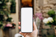 © KEA - Mockup woman's hand holding using smart phone with white blank screen POV surrounded by soft floral background, mobile app design and advertising, online marketing