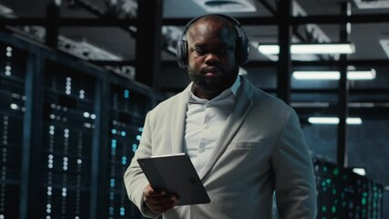 Poster - Server room programmer wearing headphones troubleshooting errors using software on tablet. IT specialist listening music, walking in data center fixing bugs using device , camera B