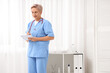 © Pixel-Shot - Happy mature female doctor with stethoscope writing on notebook in clinic