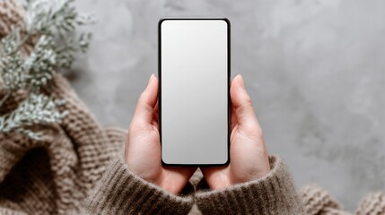 Poster - Woman Holding Smartphone with Blank Screen in Cozy Winter Setting with Knitted Sweater
