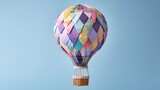 Whimsical origami hot air balloon made of pastel patchwork paper drifting against a soft sky blue background