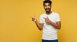 © Epic Photo - Excited Man Pointing Sideways - A young man with a joyful expression points to the side against a vibrant yellow background. He's wearing a plain white t-shirt and jeans