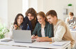 © Studio Romantic - Group of young smiling college or university students sitting at the desk in classroom and talking during a lesson discussing educational project on laptop. Education and knowledge concept.