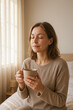 © EVISUAL - Peaceful woman with closed eyes savors warm tea in sunlit bedroom, embracing mindful slow-morning ritual and self-care, generative AI
