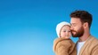 © Sweettymojidesign - Father and Child Embracing in Cozy Outfits Against a Solid Blue Sky Background