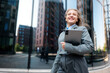© muse studio - Walking confidently through the city, a professional woman carries a tablet while enjoying the brisk air of a sunny afternoon