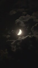 Wall Mural - The crescent moon in the first quarter phase is hidden behind clouds in the night's black sky. Clouds move quickly in the dark sky