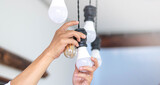 Concept of home maintenance, energy-saving, or electrical work. Hands changing a light bulb on a ceiling fixture.Multiple LED and filament bulbs hang from black sockets.