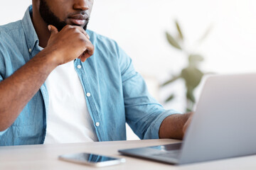 Poster - Busy Black Entrepreneur Working With Laptop At Office, Unrecognizable African Businessman Sitting At Desk, Looking At Computer Screen And Touching Chin, Closeup Shot, Cropped Image