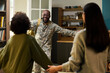 © pressmaster - Black middle aged man in military uniform entering home smiling with arms open, being greeted by Black woman and Black child, family reunion scene in domestic setting