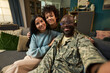 © pressmaster - Portrait of Black middle aged man in military uniform sitting on sofa with Caucasian young adult woman and multiethnic child smiling