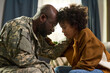 © pressmaster - Black middle aged man in military uniform comforting Black young adult woman at home, both sitting close with foreheads touching, showing emotional family support and connection