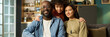© pressmaster - Portrait of middle aged Black man in casual clothing sitting with smiling multiethnic teenager and young adult Caucasian woman at home, all looking at camera, showing family unity