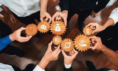 Poster - A diverse group of professionals unites hands around wooden gears, symbolizing collaboration and strategic planning for enhanced business efficiency and successful outcomes. Amity