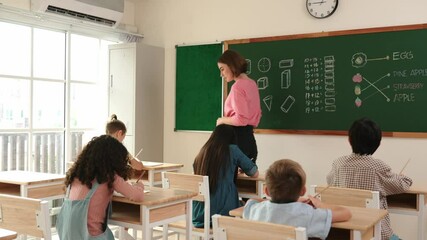Poster - Smart teacher checking cute student homework while explaining idea at class. Attractive instructor walking around classroom while looking at notebook and talking about Math theory to child. Pedagogy.