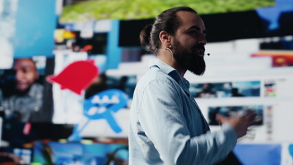 Poster - With a hands free microphone, male trend setter hosts a live presentation offering insight for innovation. Speaker discussing with the audience about online entertainment. Camera A.