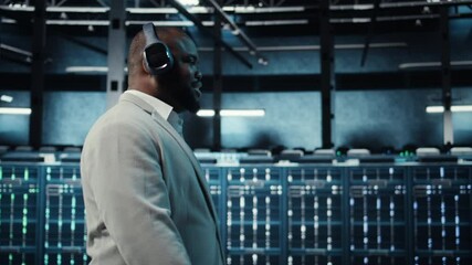 Poster - Happy worker wearing headphones walking in data center with hardware used to host websites. Cheerful IT expert listening music while overseeing dimly lit server farm rigs, camera A