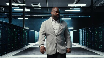 Poster - Employee walking in data center with blinking lights on rigs showing system activity. IT professional overseeing dimly lit server farm with equipment arranged for smooth operations, camera A