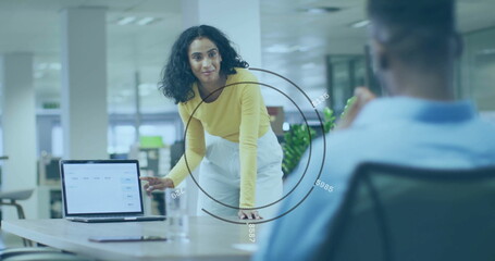 Poster - Leaning forward woman in yellow top presenting data on laptop at office desk, with potted plant