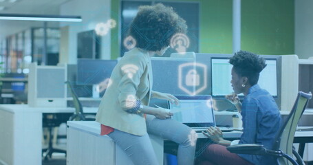 Poster - Examining security icons on laptops, two professionals leaning over desk in modern open-plan office