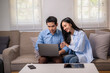 © Apichat - A man and woman are sitting on a couch looking at a laptop