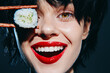 © VICHIZH - Happy young woman holding sushi with chopsticks, smiling joyfully against a dark background, showcasing vibrant colors and an expressive, playful mood.
