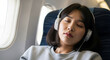 © minwoo Jung - 비행기 안에서 헤드폰을 끼고 눈을 감고 휴식 중인 젊은 여성
