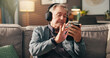 © peopleimages.com - Senior man, phone and listening to music with headphones on sofa for online streaming at home. Elderly, male person or user with mobile smartphone for podcast, radio news or entertainment at house