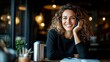 © svastix - A happy woman with curly hair sits at a cozy coffee shop, smiling while holding a pen, radiating warmth and approachability in a casual, inviting atmosphere for lifestyle photography.