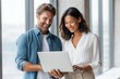 © Lady O - Handsome Caucasian man with brown hair and a blue shirt is showing his laptop screen to a beautiful Asian woman in a white blouse.
