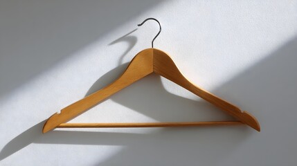 Poster - A simple wooden clothes hanger suspended on a plain white wall creating a clean and minimalist composition with soft shadows