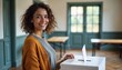 © AiGalaxy - Smiling young woman with curly hair stands beside a ballot box in a bright room. She wears a gray shirt and orange cardigan, ready to vote.